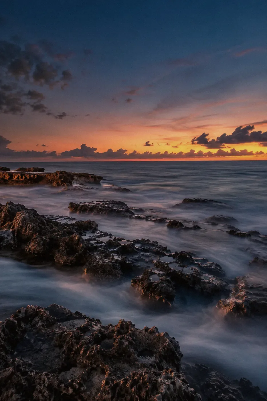 Blue-hour ocean washing over dark coastal rocks